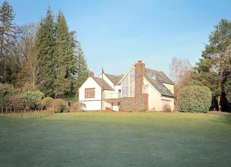 A twin-gabled house overlooks a large lawn bordered by a tall hedge.