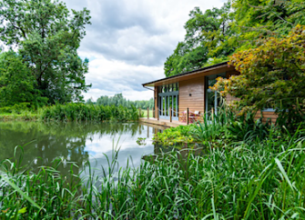 A secluded wooden holiday lodge with large windows overlooks a riverbank.