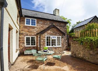 Exterior of a stone-built cottage overlooking a paved courtyard with dining table and chairs.