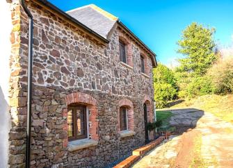 Stone-built, 2-storey Devon barn conversion by a paved courtyard and hedgerow.