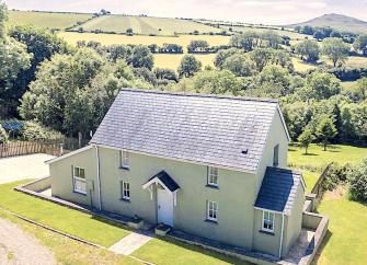 Aerial photo of a detached cottage surrounded by lawns and open countryside