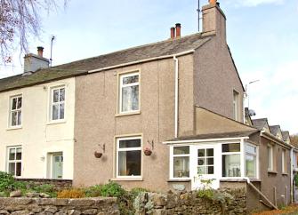 A semi-detached cottage with enclosed front porch and a front garden behind a low stone wall.