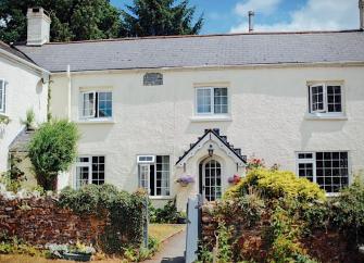 A large Exmoor farmhouse with cottage windows and covered porch sits behind a walled front garden.