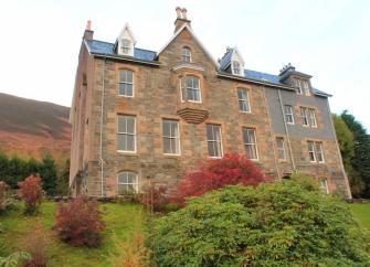 Exterior of a grand 3-storey Highland hunting lodge and gardens.