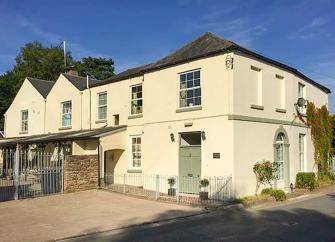A large, rendered Hereford holiday home with large sash windows overlooks a spacious paved courtyard.