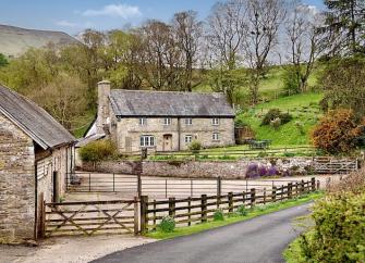 A pair of slate-roofed stone cottages in Herefordshire with large gardens overlook a country lane.
