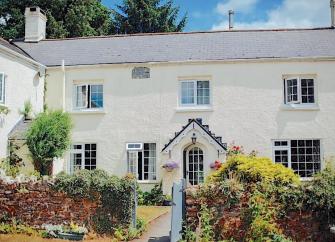 Large Exmoor farmhouse with cottage windows and a covered porch sits behind a walled front garden.