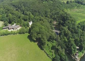 Aerial photo of a large holiday home nestling between mature woodland and fields overlooking a wide river.