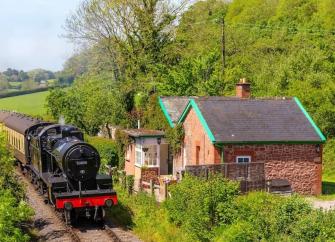 A steam-train passes by a line-side holiday cottage on a sunny summer's day.