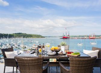 An outdoor table laid for dinner on a deck overlooks a boat-filled Falmouth Estuary.