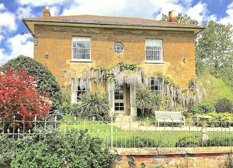 Exterior of a wisteria-clad, double-fronted Georgian House and front garden.