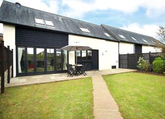 A semi-detached, part-timbered contemporary cottage with bi-fold windows, patio and a spacious lawn.