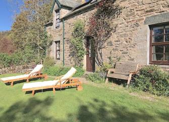 Sun loungers on a lawn in front of a stone-built holiday cottage