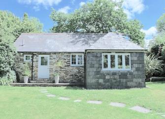 The granite-built exterior of a single-storey Cornish holiday home surrounded by lawns.