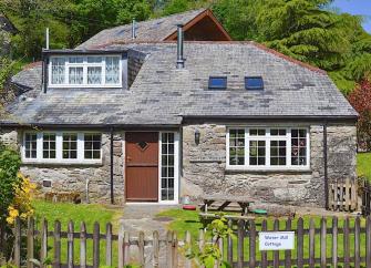 Exterior of a stone-built rural holiday cottage surrounded by lawns.