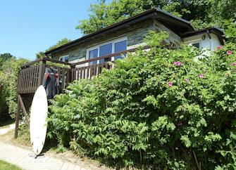 Exterior of a single-storey cottage surrounded by trees and flowering shrubs.