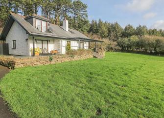 A North Cornwall holiday lodge with sheltered frontage overlooks grass field.