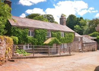 Exterior of a bushy, ivy-clad Dartmoor farmhouse.