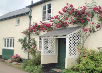 Climbing roses surround the porch of a country cottage in Somerset.