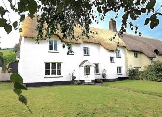 Exterior of a thatched Exmoor cottage overlooking a large lawn.