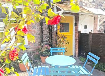 A leafy courtyard with a table and chairs in front of a stone-built Somerset coastal cottage.