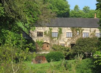 A country cottage with a backdrop of mature trees and a large front garden.