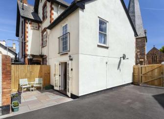 Exterior of a 2-storey cottage with courtyard and large tarmac parking space.