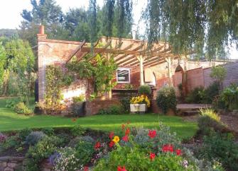 The exterior of a single-storey holiday apartment with a vine-covered pergola and floral garden.