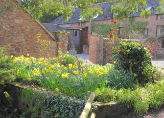 Exterior of a stone-built holiday home in Dunster surrounded by a stone wall..