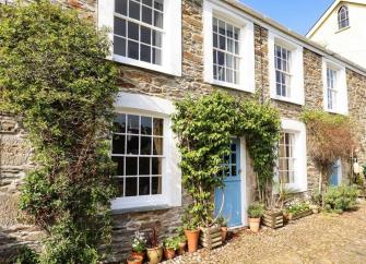 Exterior of a wisteria-clad, terraced holiday cottage in Mevagissey overlooking a cobbled street.