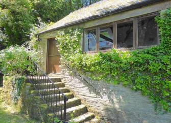 The leafy-clad exterior of a stone-built single-storey Exmoor holiday cottage with a flight of stone steps to the front door.