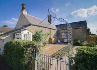 An L-shaped, stone-built, village cottage surrounded by a tidy garden.