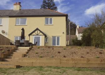 The exterior of a double-fronted house with a patio containing dining furniture  2.