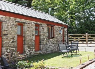 A single storey, stone barn conversion overlooks a lawned garden with outdoor table and chair.