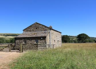 A fenced-in stone-built barn conversion is surrounded by open fields