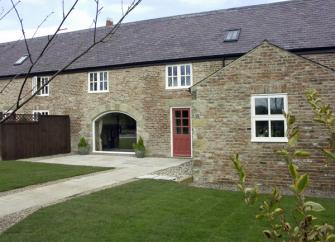 Two-lawns and a path ead to a stone-built terraced cotage with a foor-to-ceiling wide front window.