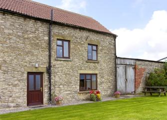 A stone-built, 2-storey holiday cottage in Helmsley overlooking a large lawn.