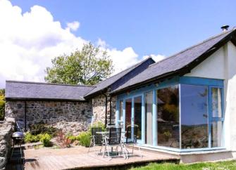 Exterior of a single-storey, stone barn conversion with a contemporary wood and glass extension.