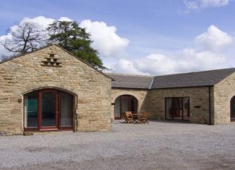 A U-shaped, stone barn conversion with floor-to-ceeiing windows looks out over a large shingled courtyard.