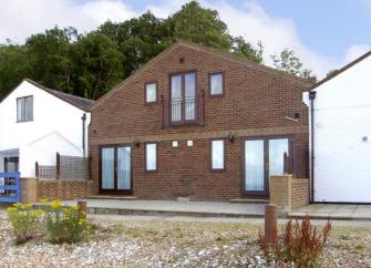 A wide 2-storey gable end of an Isle-of-Wight holiday cottage with floor-to-ceiling windows.