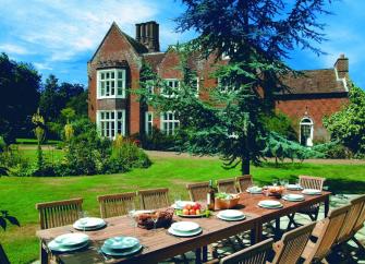 A large rectory and coach house overlooks a lawn with a table laid for lunch.