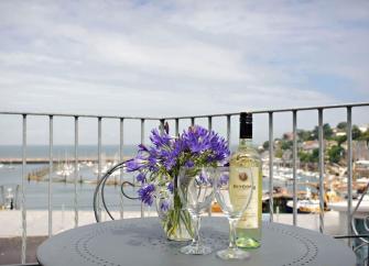 Behind a table set for cocktails on a balcony is a view of Brixham Harbour.