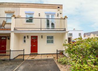 A semi-detached with a large 1st floor balcony overooks a front garden with off-road parking.