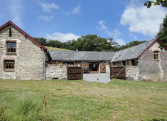 A twin-gabled Exmoor barn conmverion surounded by a lawn.