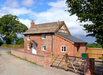 A red brick Herefordshire holiday cottage with a ground floor extension is surrounded by a low tone wall