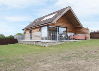 A large wooden Somerset holiday lodge with a hot tub on a sheltered deck overlooking a spacious lawn.
