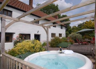 A hot tub under a pergola sits in front of a large 2-storey, Somerset farmhouse.