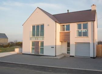 A modern detached house with large windows and space for off-road parking in front.