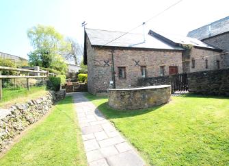 A large Exmoor Farm Cottage overlooks a lawn surrounded by a stone wall.