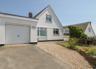A chalet bungalow and twin garage overlook a sloping front lawn and tarmac driveway